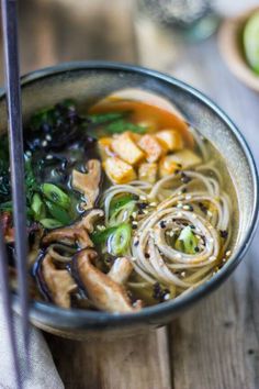 a bowl filled with noodles and vegetables next to chopsticks on a wooden table