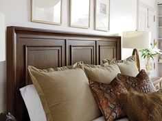 a bed topped with lots of pillows next to two framed pictures on the headboard