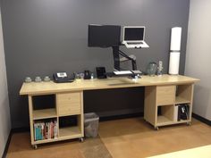 a computer desk with two monitors and a keyboard on it in an office space that is painted gray