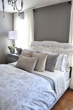 a bed with white and gray comforters in a bedroom next to a chandelier