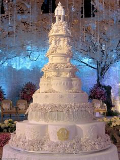 a large white wedding cake sitting on top of a table next to flowers and chandeliers