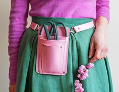 a woman wearing a green skirt with pink flowers in her pocket and holding a pink purse