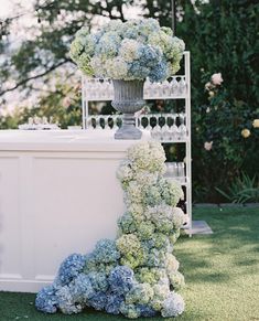 a tall vase filled with blue and white flowers on top of a grass covered field