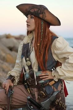 a woman with red hair wearing a pirate costume sitting on the rocks by the water