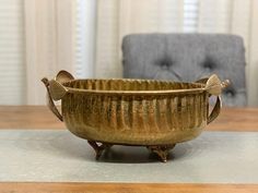 a metal bowl sitting on top of a wooden table next to a gray chair in front of a window