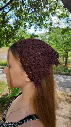 a woman with long hair wearing a brown crochet headband in front of a tree