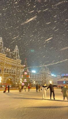 people are standing in the snow near a large building with lights on it's sides