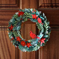 a paper wreath with a cardinal on it hanging from a wooden door handle, decorated with holly and red flowers