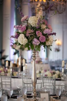 a tall silver vase filled with lots of purple and white flowers on top of a table