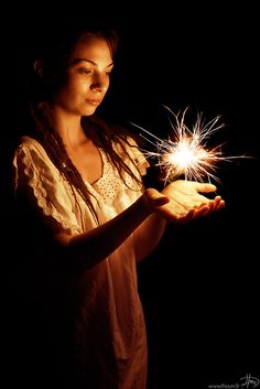 a woman holding sparklers in her hands on a dark background with only one light visible