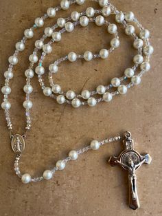 This Wedding Gift Rosary symbolizes the unity of marriage between the bride and groom and the union of the two becoming one in Christ. What great blessings it gives to that special couple and their new life together! This elegant pearl glass bead rosary was made handmade in the USA using 10mm White Pearl glass beads with Czech fire-polished AB crystal glass accent beads, and your choice of Our Father beads (pearl beads or Mother of Pearl Cross), your choice of rosary center and if you want metal end caps on the pearl beads.  A gorgeous 3" silver Benedictine crucifix completes the rosary beautifully. The length of the rosary hanging up is 31 inches from top to bottom. Comes in a velvet drawstring bag. White Hand-strung Wedding Necklaces, White 8mm Beads Jewelry For Anniversary, White Hand-strung Necklaces For Wedding, Hand-strung Pearl Wedding Necklaces, Hand-strung Pearl Necklaces For Weddings, Spiritual Beaded Jewelry For Anniversary, Pearl White 8mm Beads Wedding Jewelry, Adjustable Elegant Rosary, Hand-strung Pearl White Jewelry For Wedding