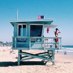 a lifeguard stand on the beach with people in the water and an american flag hanging from it