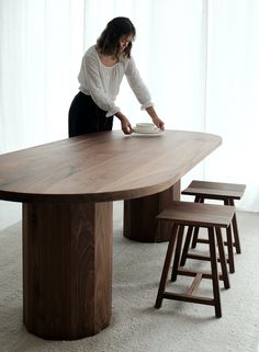 a woman standing at a wooden table with stools