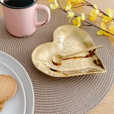 two heart shaped cookies on plates next to a pink coffee cup and saucer with yellow flowers in the background