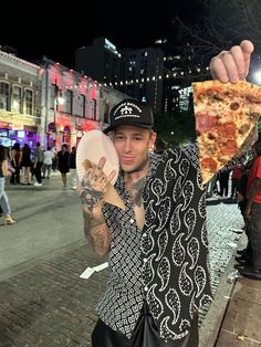 a man holding up a slice of pizza in the middle of a street at night