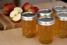 four jars filled with honey sit on a cutting board next to apples