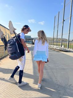 a man and woman walking down a sidewalk holding hands while wearing baseball uniforms on the other side