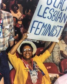 a woman holding up a sign in the middle of a room with people sitting and standing around