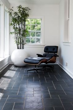 an eames chair and ottoman sit in the corner of a room with large windows