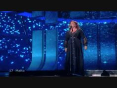 a woman standing on top of a stage in front of a microphone and wearing a long black dress