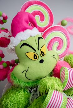 a green stuffed animal with a pink hat on it's head sitting in front of christmas decorations