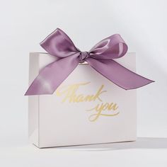 a white box with a purple ribbon and thank you written on the front in gold foil