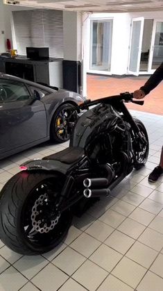 a man standing next to a black motorcycle in a garage with two other cars behind him