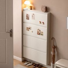 a white cabinet sitting in the corner of a room next to a door with shoes on it