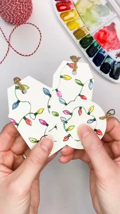 two hands holding small cards with colorful flowers on them and watercolors in the background