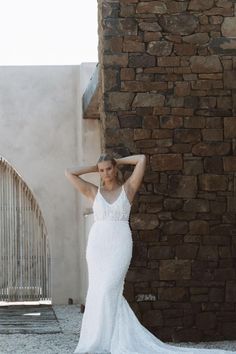 a woman in a wedding dress leaning against a stone wall with her hand on her head