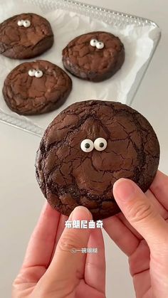 a person holding up a chocolate cookie with eyes and googly eyes in front of them