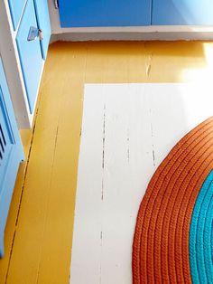 an orange and blue rug sitting on top of a wooden floor next to a cabinet