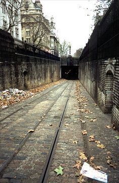 a train track going into a tunnel with leaves on the ground and buildings in the background