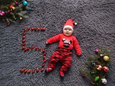 a baby wearing a santa hat laying on the floor next to a christmas tree and decorations