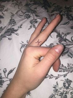 a person's hand with a small cross tattoo on the middle finger, laying in bed