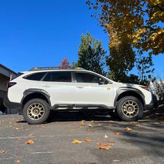 a white subarunt parked in front of a house with autumn leaves on the ground