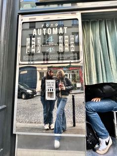 two people sitting on a bench in front of a window with an automat sign