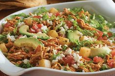 a salad with chicken, avocado and tomatoes in a white casserole dish