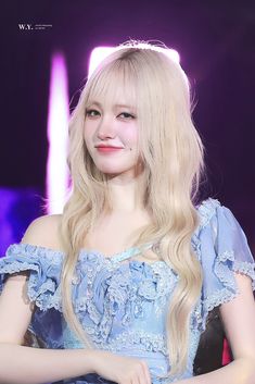 a woman with long blonde hair wearing a blue dress and smiling at the camera while sitting down