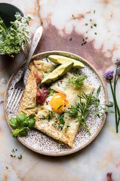 a plate with an egg, avocado and bread on it next to some flowers