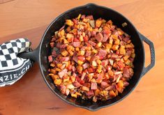 a skillet filled with food sitting on top of a wooden table next to oven mitts