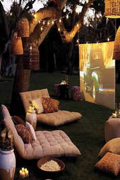 an outdoor movie is set up in the grass with lights strung over it and pillows on the ground