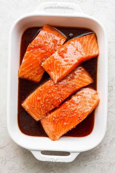 salmon fillets in a white casserole dish with brown sauce on the side