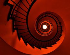 a spiral staircase with red light coming from the top to the bottom in a dark room