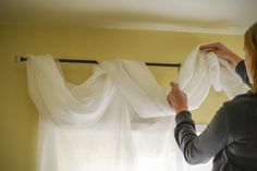 a woman hanging curtains in front of a window