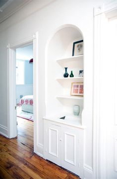 an empty room with white walls and wood flooring is pictured in this image, there are shelves on either side of the door