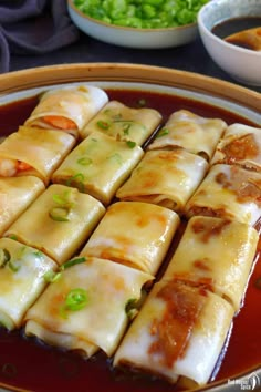 rice noodle rolls in a bowl with sauce and green onions on the side, ready to be eaten