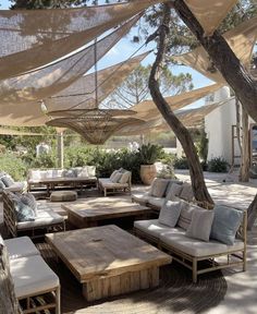 an outdoor seating area with tables and couches under a canopy over the patio, surrounded by trees