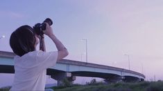 a woman is looking through binoculars on the side of a road near a highway bridge