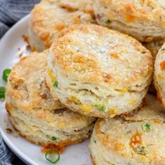 several biscuits are stacked on top of each other in a white plate with green onions